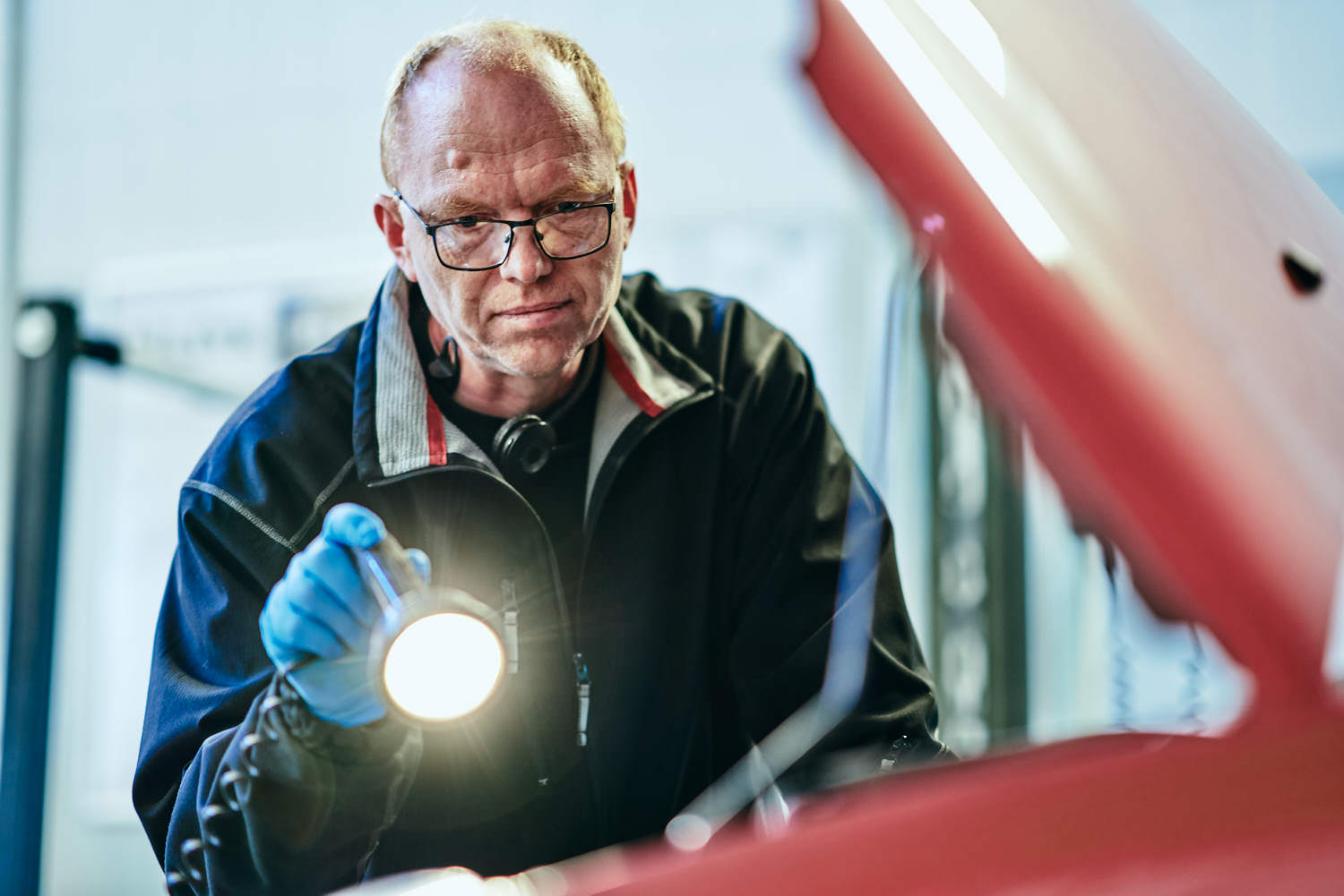 Synsmand gennemgår motorrummet med lygte ved bilsyn i Odense